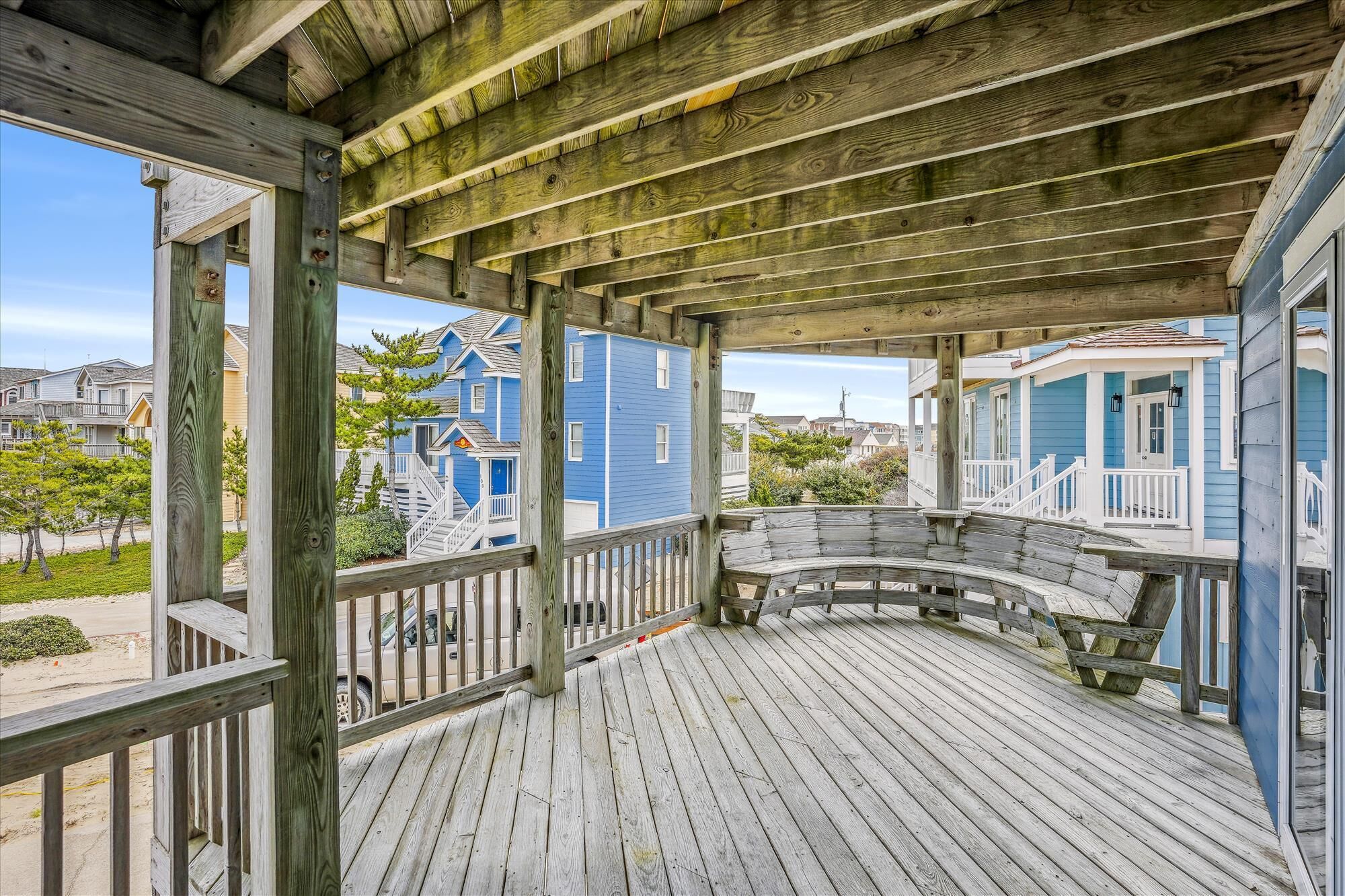 A wooden deck with a curved bench, a railing, and a view of blue houses.