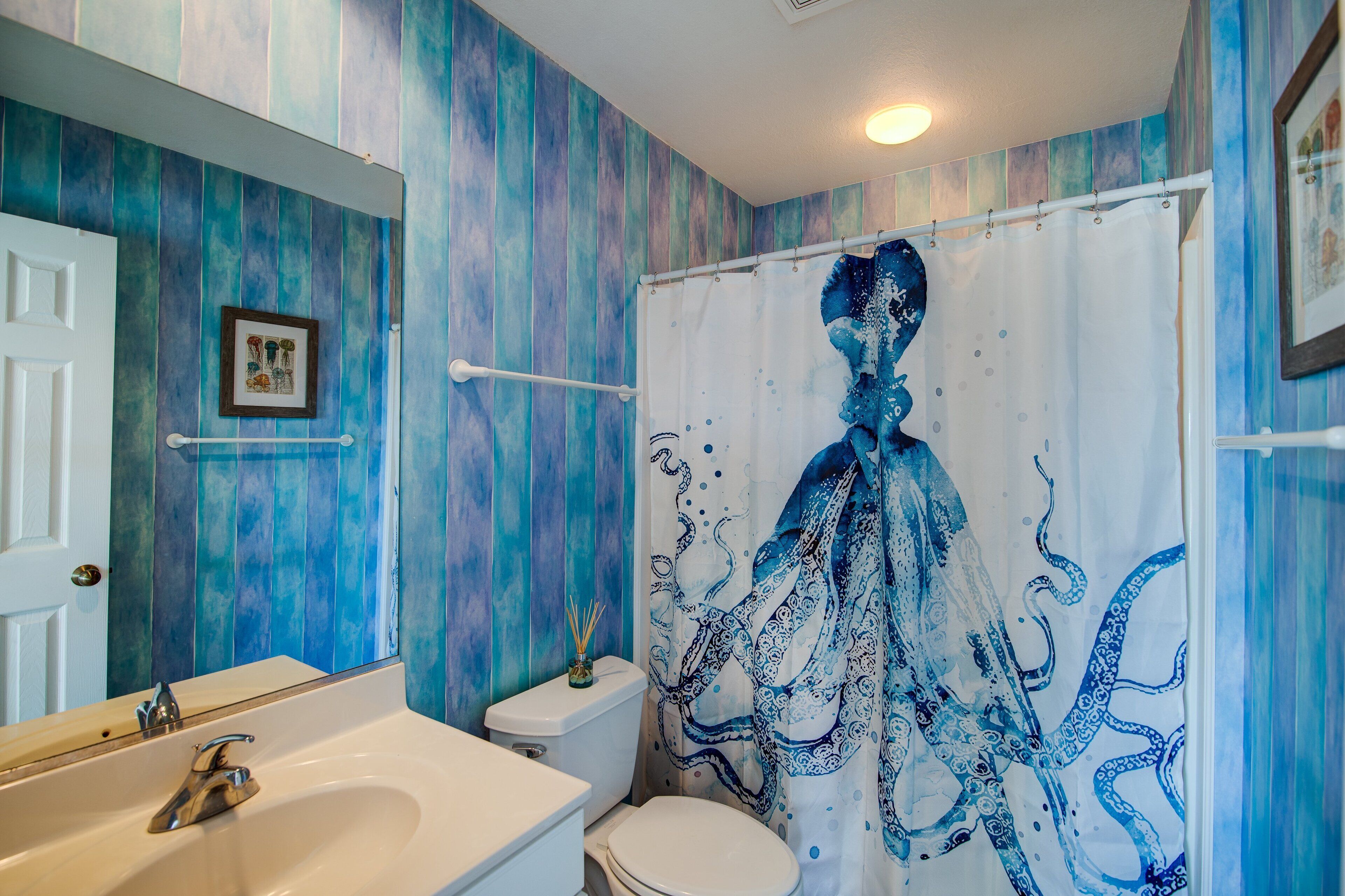 A bathroom with a blue and white color scheme, a shower curtain with an octopus design, a white toilet, and a sink with a mirror above it.