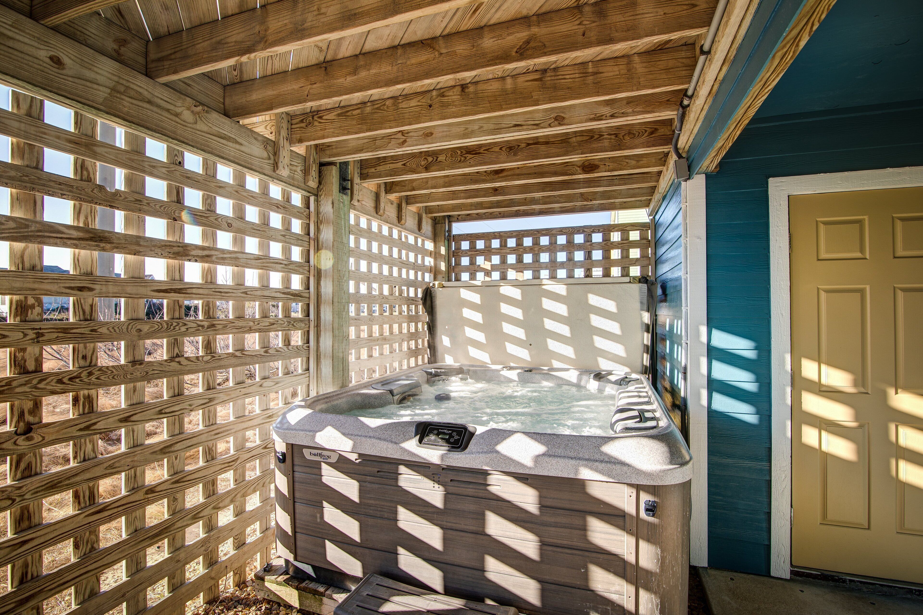A wooden deck with a hot tub, a wooden fence, and a blue door.