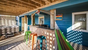 A covered outdoor area with a wooden ceiling, a bar area with stools, and a view of the ocean through a window.
