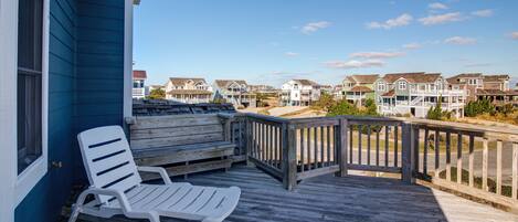 A wooden deck with a white lounge chair, overlooking a row of houses with a clear blue sky.