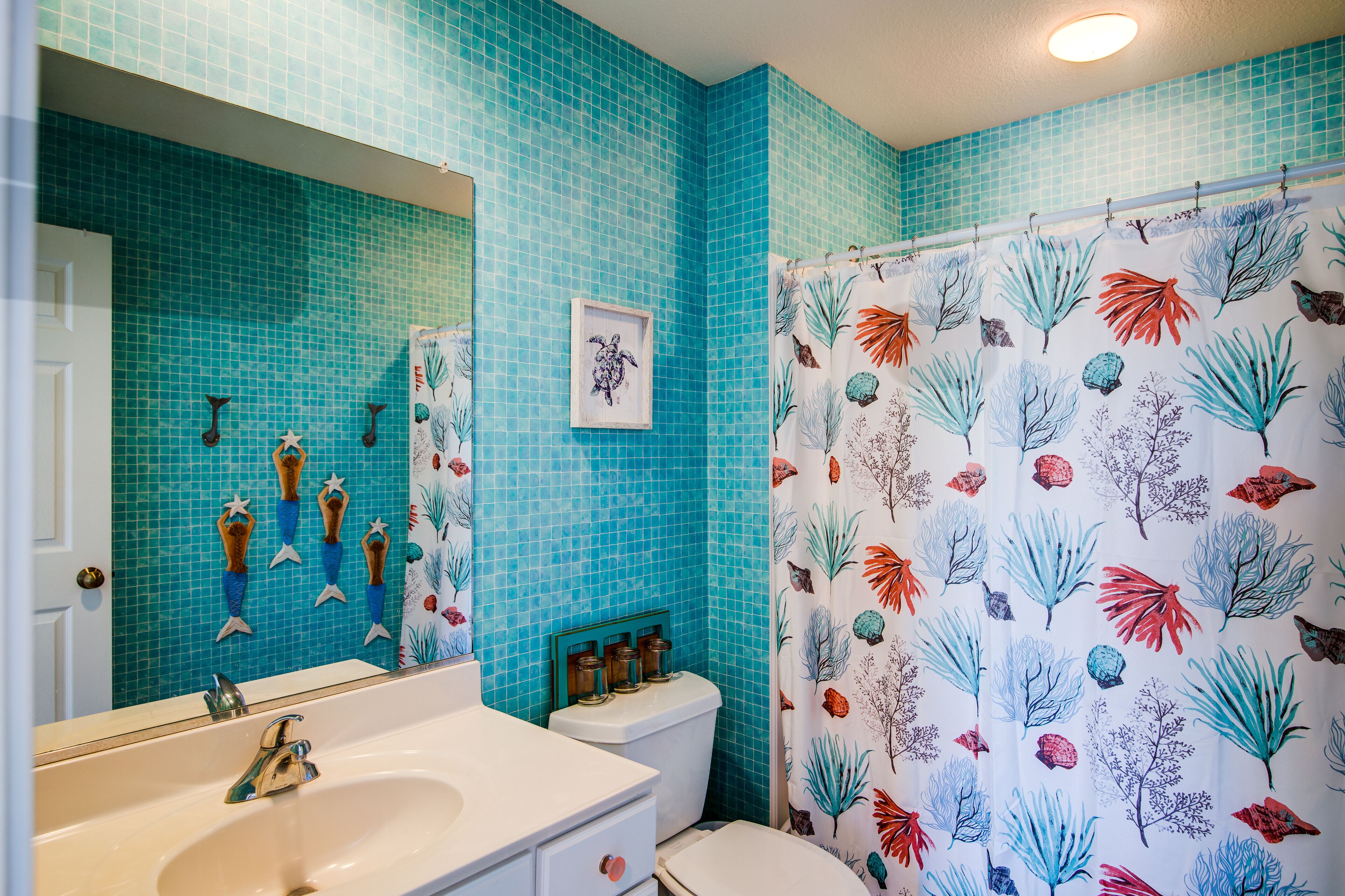A bathroom with blue tiled walls, a white sink, a toilet, and a shower curtain with a leaf pattern.