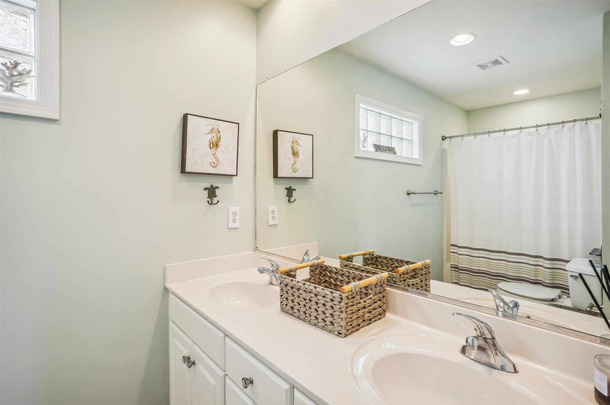 A bathroom with two sinks, a large mirror, and framed artwork on the wall.