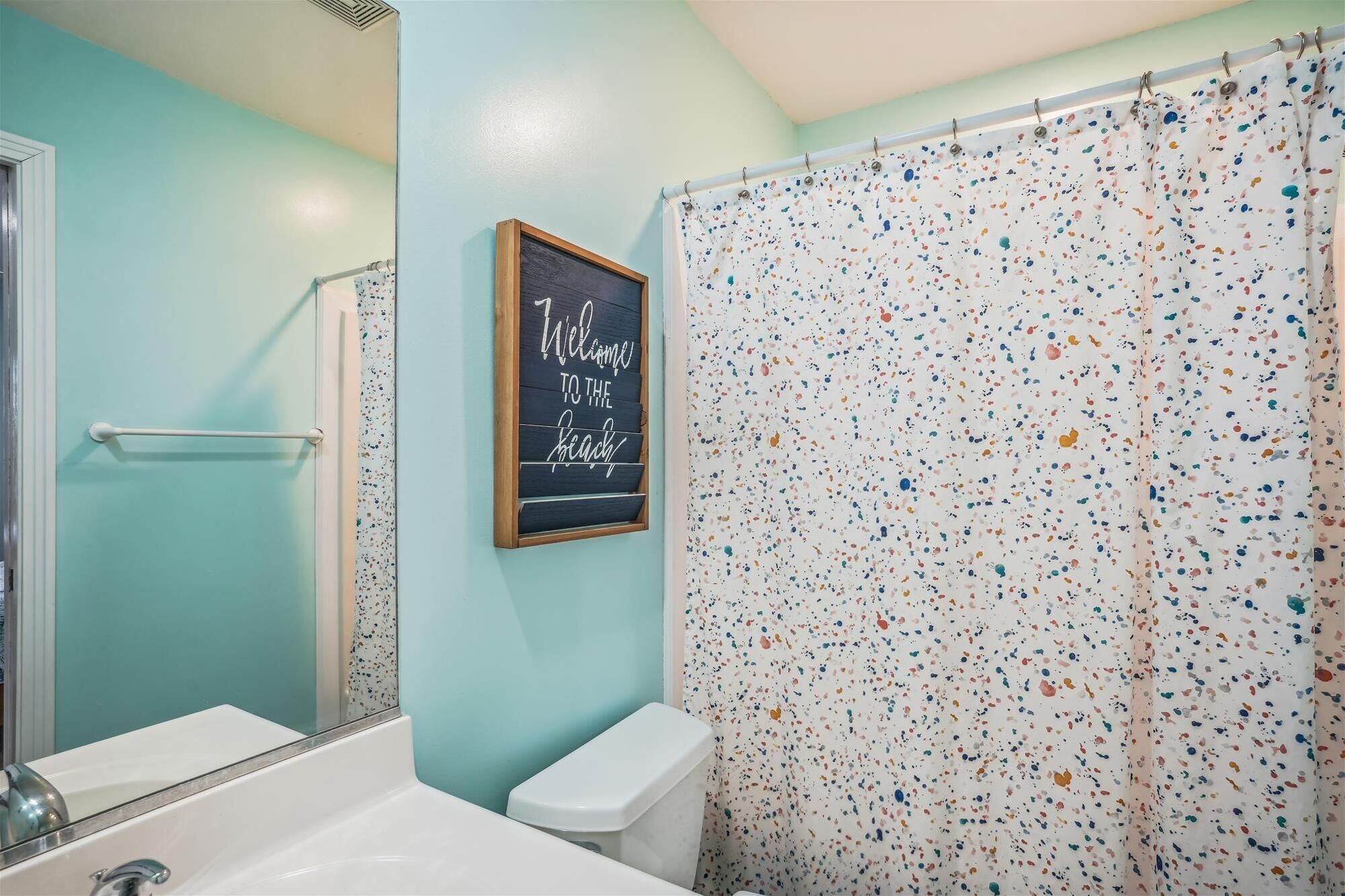Une salle de bain avec un mur de couleur turquoise, une baignoire blanche, des toilettes blanches et un rideau de douche à motifs pointillés.