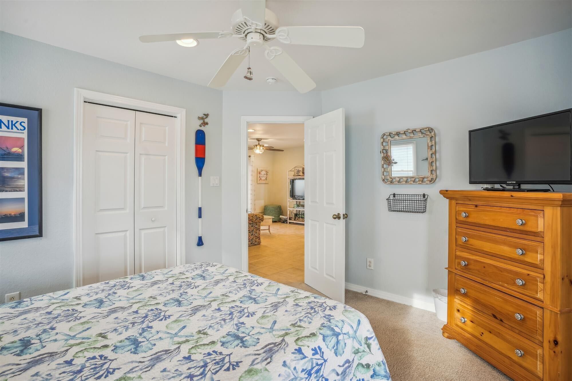 A bedroom with a bed, a wooden dresser, a ceiling fan, and a television.