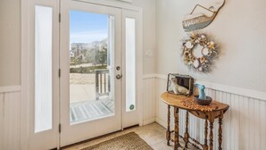 A front door with a view of a residential area, a wooden console table with decorative items, and a 'Welcome' sign on the wall.