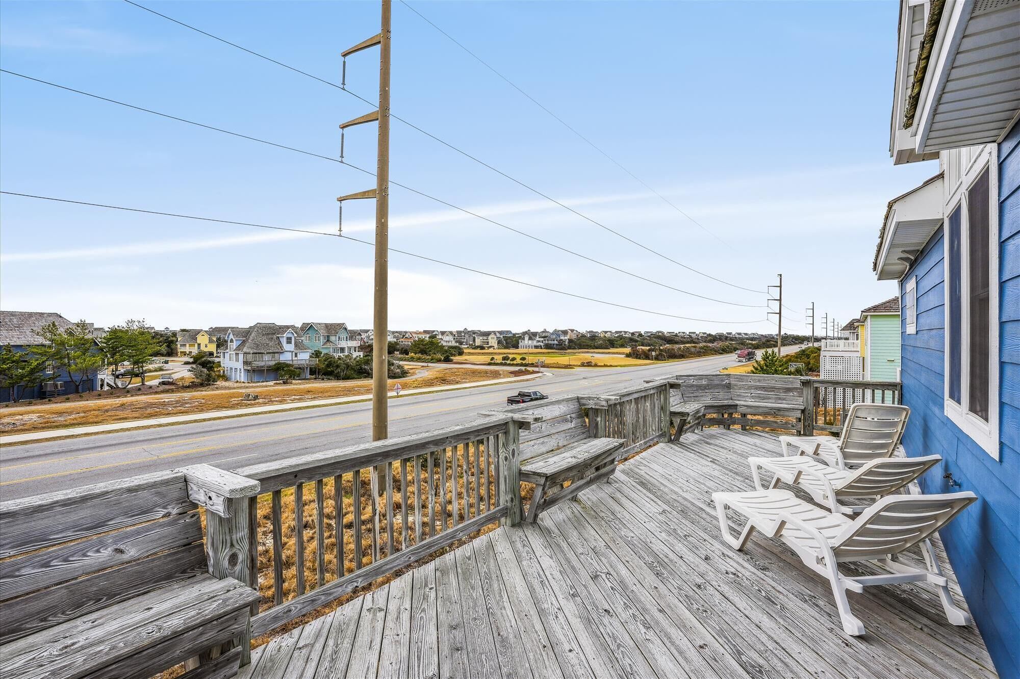 A wooden deck with white lounge chairs and a view of a road and houses in the distance.