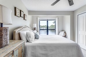A bedroom with a large bed, a wooden dresser, a ceiling fan, and a window with curtains.