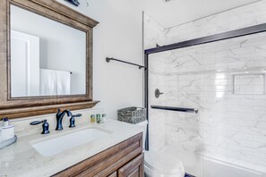 A bathroom with a marble sink, wooden vanity, and a glass shower enclosure.
