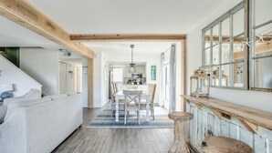 Un vaste espace de vie comprenant un canapé, un plancher en bois et une table à manger avec des chaises. On peut également admirer une charpente en bois et un tabouret en bois rustique.