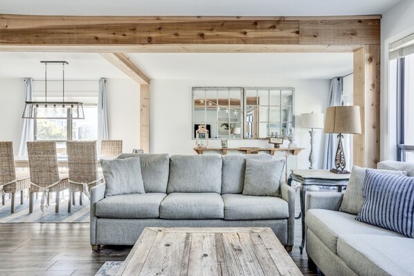 A living room with a grey sofa, wicker chairs, a wooden coffee table, and a large mirror above a wooden table.