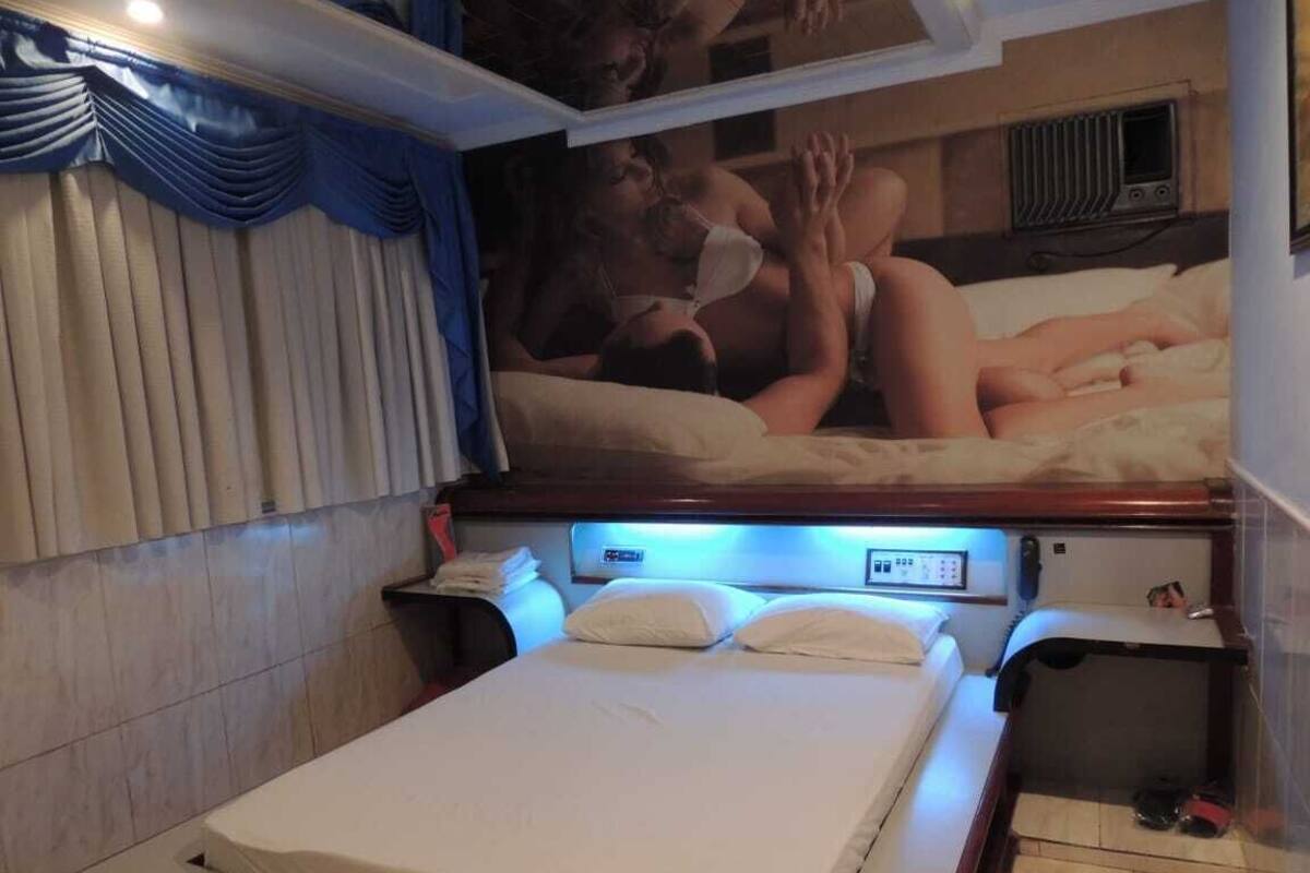 A hotel room with a bed, a nightstand, a bedside table, and a wall-mounted air conditioning unit.