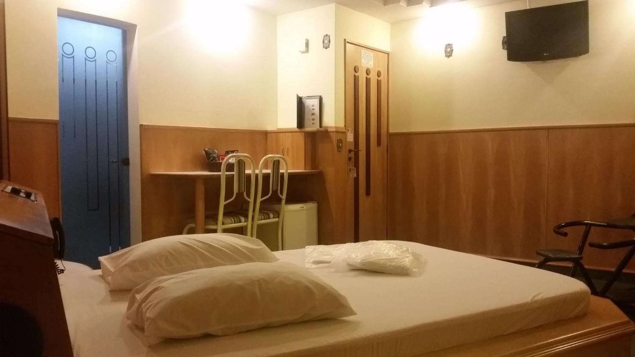 A hotel room with a bed, a desk, a chair, a wardrobe, and a television on the wall.