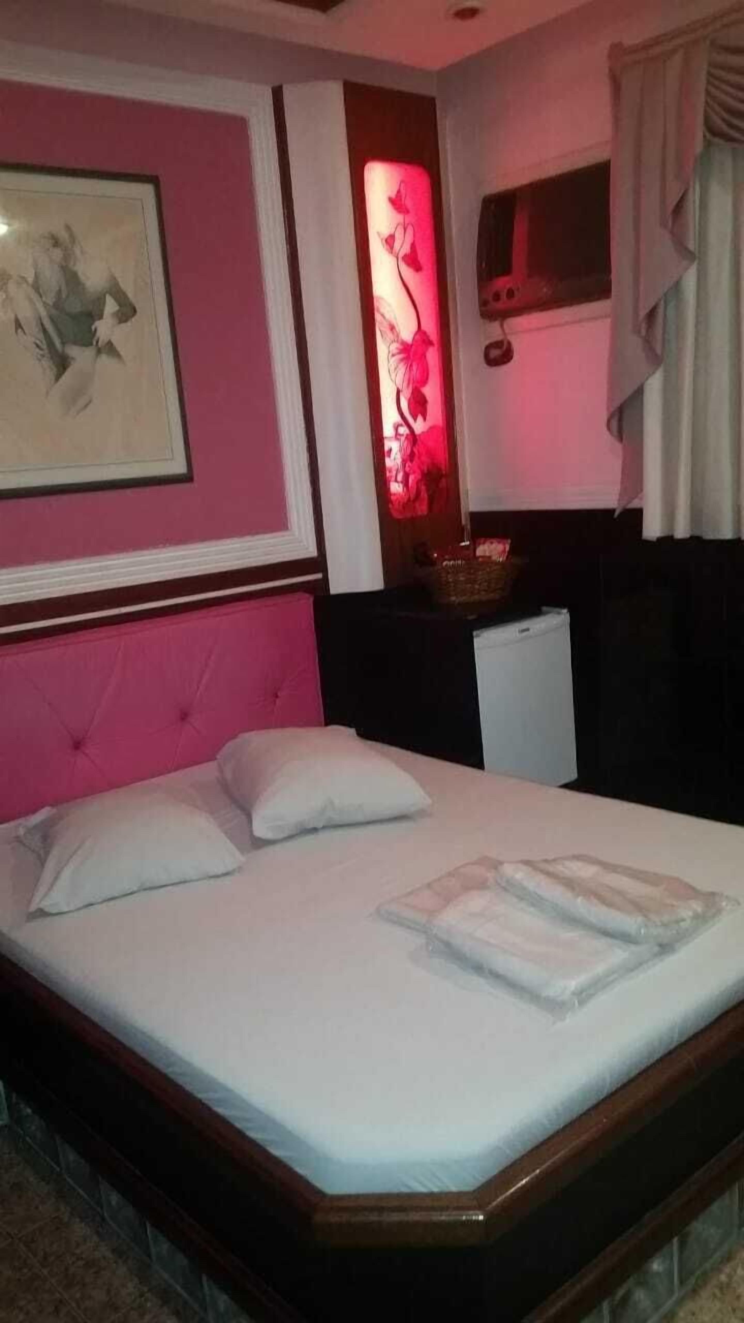 Un dormitorio con cama, mesita de noche, lámpara de pared y un cuadro enmarcado.