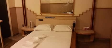 Une chambre d’hôtel comprenant un lit, deux tables de chevet, une commode, un miroir et une horloge murale.