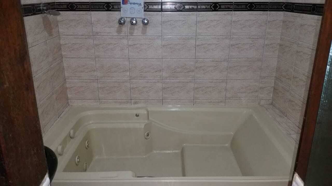 Casa de banho com banheira, paredes revestidas a azulejo e um chuveiro.