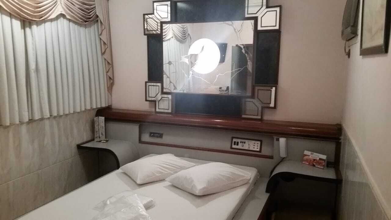 A hotel room with a bed, two bedside tables, a mirror, and a window with curtains.