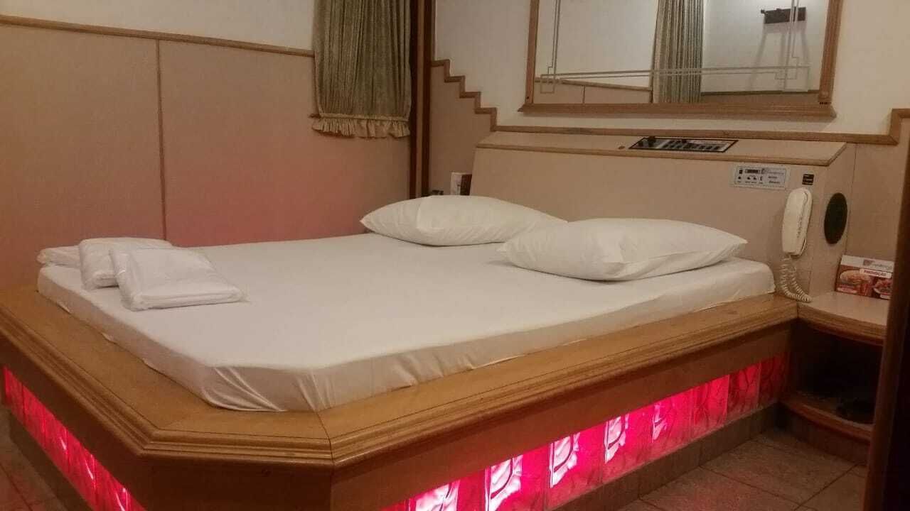 A neatly made bed with white linens and pillows, a bedside telephone, and a small shelf with a box.