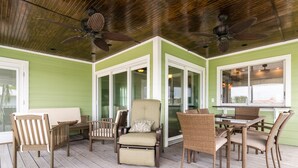A covered outdoor area with a wooden deck, wicker furniture, and ceiling fans.