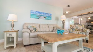 A living room with a beige sofa, a wooden coffee table, and a painting of a pier.