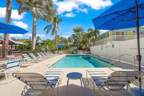 Relax by the serene pool surrounded by lounge chairs and umbrellas, shaded by tall palm trees.