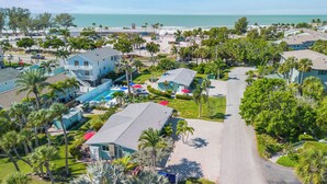 Vue aérienne d’un quartier résidentiel situé sur la côte, avec des maisons, une piscine et une plage en arrière-plan.