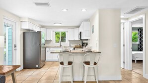 Une cuisine moderne avec des meubles blancs, un îlot central et deux tabourets de bar.