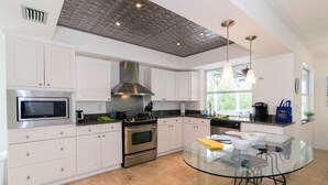 Una cocina moderna con armarios blancos, electrodomésticos de acero inoxidable y una mesa de comedor de vidrio.