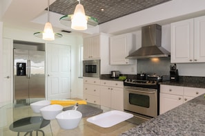 Una cocina moderna con armarios blancos, electrodomésticos de acero inoxidable y una mesa de comedor de vidrio.