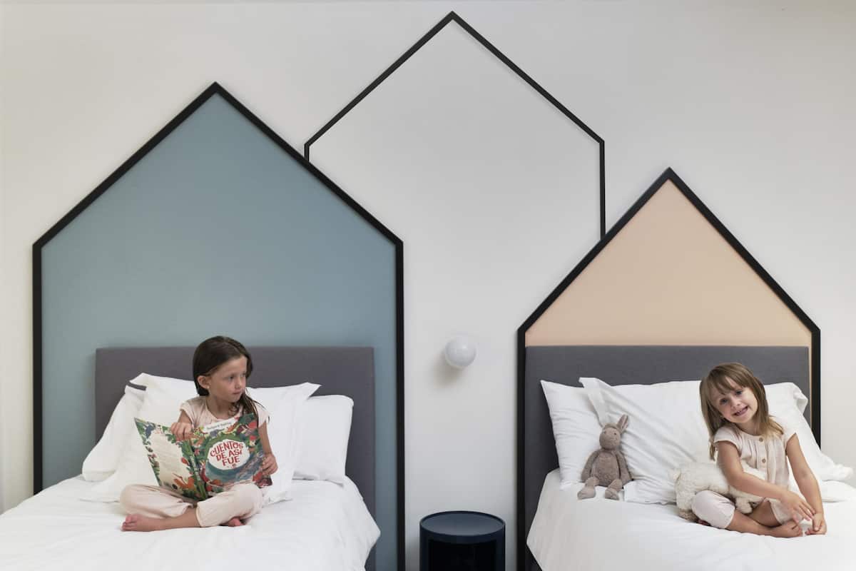 Two beds with geometric headboards, a round nightstand, and a wall-mounted light fixture.
