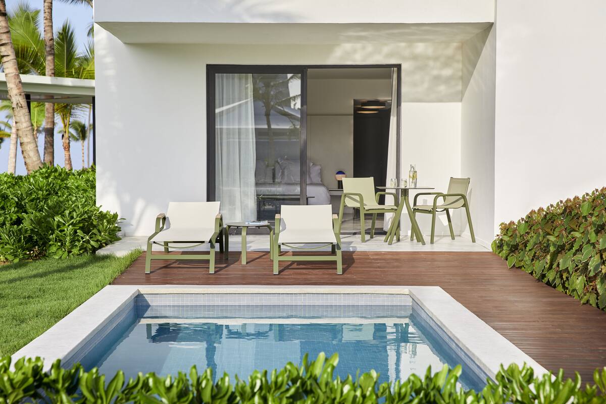 A modern outdoor pool area with a wooden deck, lounge chairs, and a glass door leading to a room.