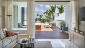 Een moderne woonkamer met een bank, een bijzettafeltje met drankjes, en uitzicht op een terras met tuinmeubels en palmbomen.