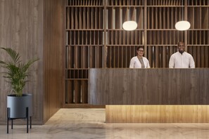 A reception desk with a wooden panel backdrop, a potted plant, and a marble floor.
