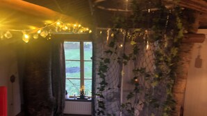 A rustic interior with a wooden ceiling, a window with a view of a green landscape, and a net-covered wall with hanging lights. - Treehouse Magpies Nest With Bubble Pool (Avesta)