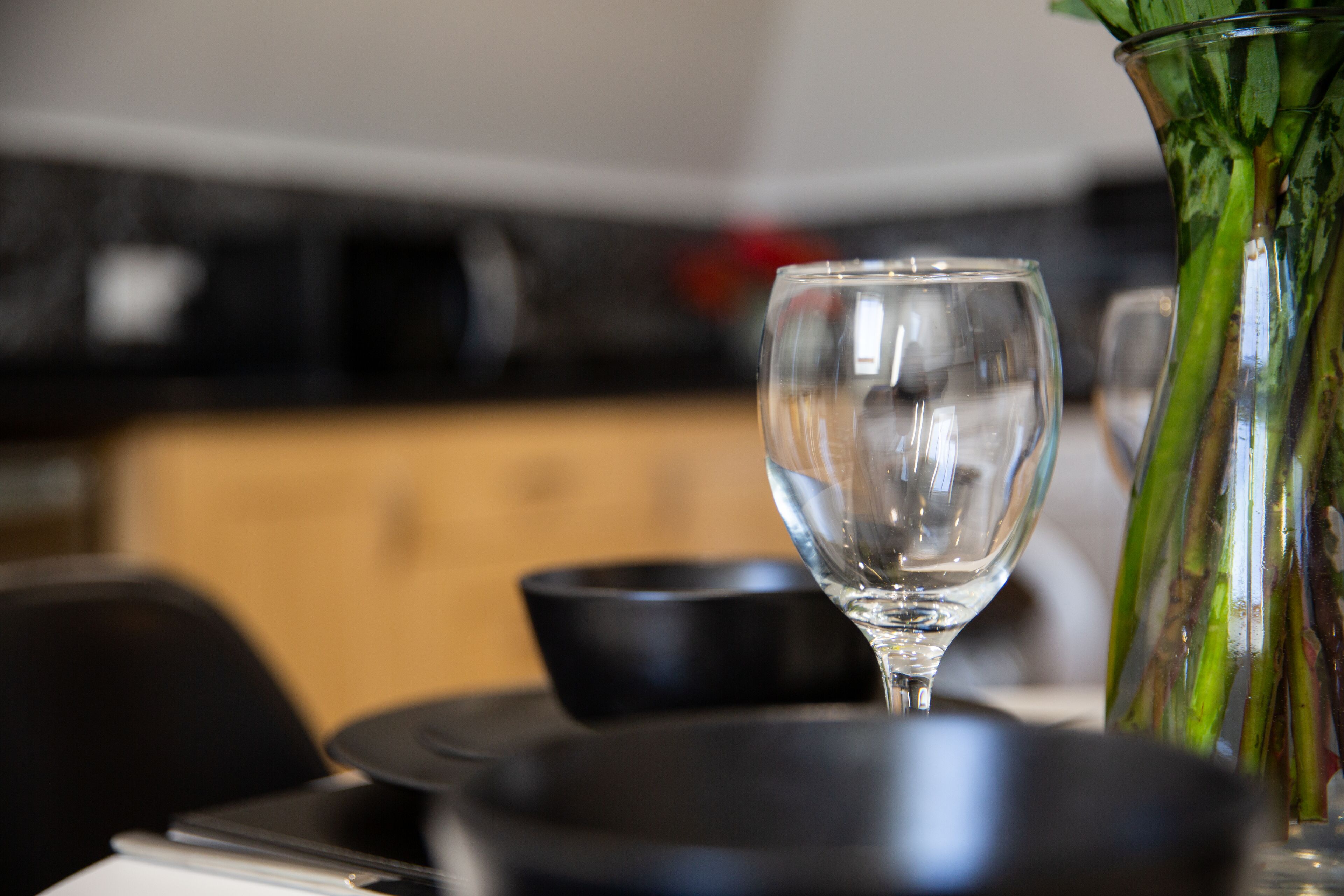 Une table à manger avec un verre à vin en verre transparent et un vase contenant des tiges vertes.