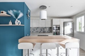 A modern kitchen with a central island, bar stools, a built-in oven, and a refrigerator.