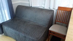 Una stanza compatta con un divano grigio e una sedia in legno.