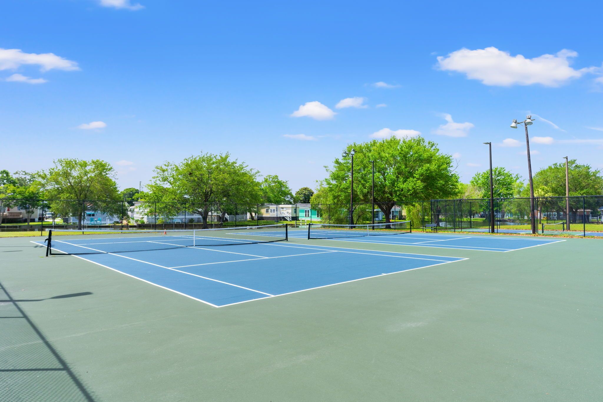 A tennis court with a net, surrounded by trees and a fence.