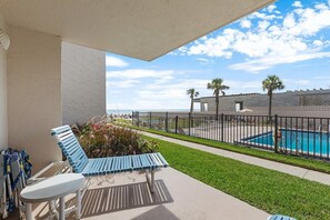 Un balcón con sillones de descanso, una piscina y vista al océano.