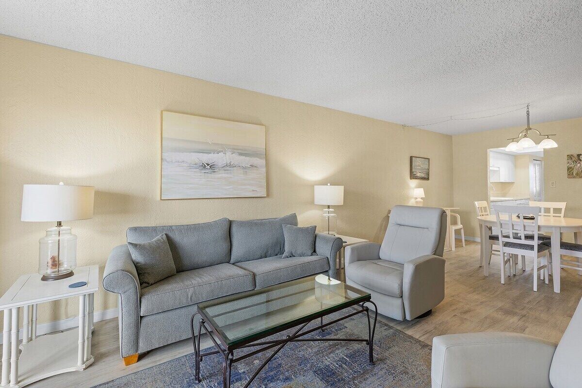 Un salon comprenant un canapé, un fauteuil, une table basse en verre et un coin repas avec une table et des chaises.