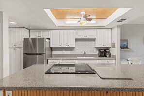 A modern kitchen with white cabinets, a stainless steel refrigerator, a built-in oven, and a granite countertop.