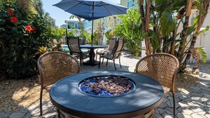 An outdoor patio with a stone fire pit, wicker chairs, and a table with chairs.