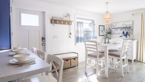 A bright, airy dining area with a white table set for four, a blue door, and a view through a window.