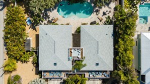 An aerial view of a resort with two large buildings, a central swimming pool, and surrounding palm trees.