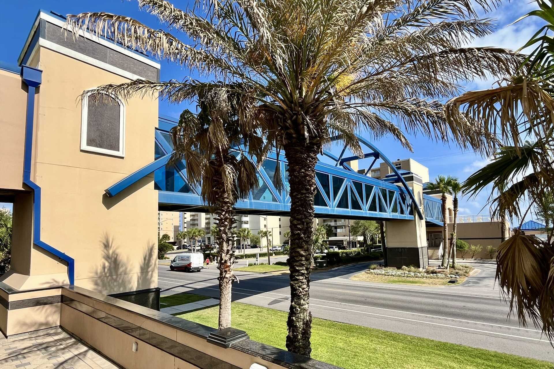 A modern building with a blue bridge structure, palm trees, and a clear sky.