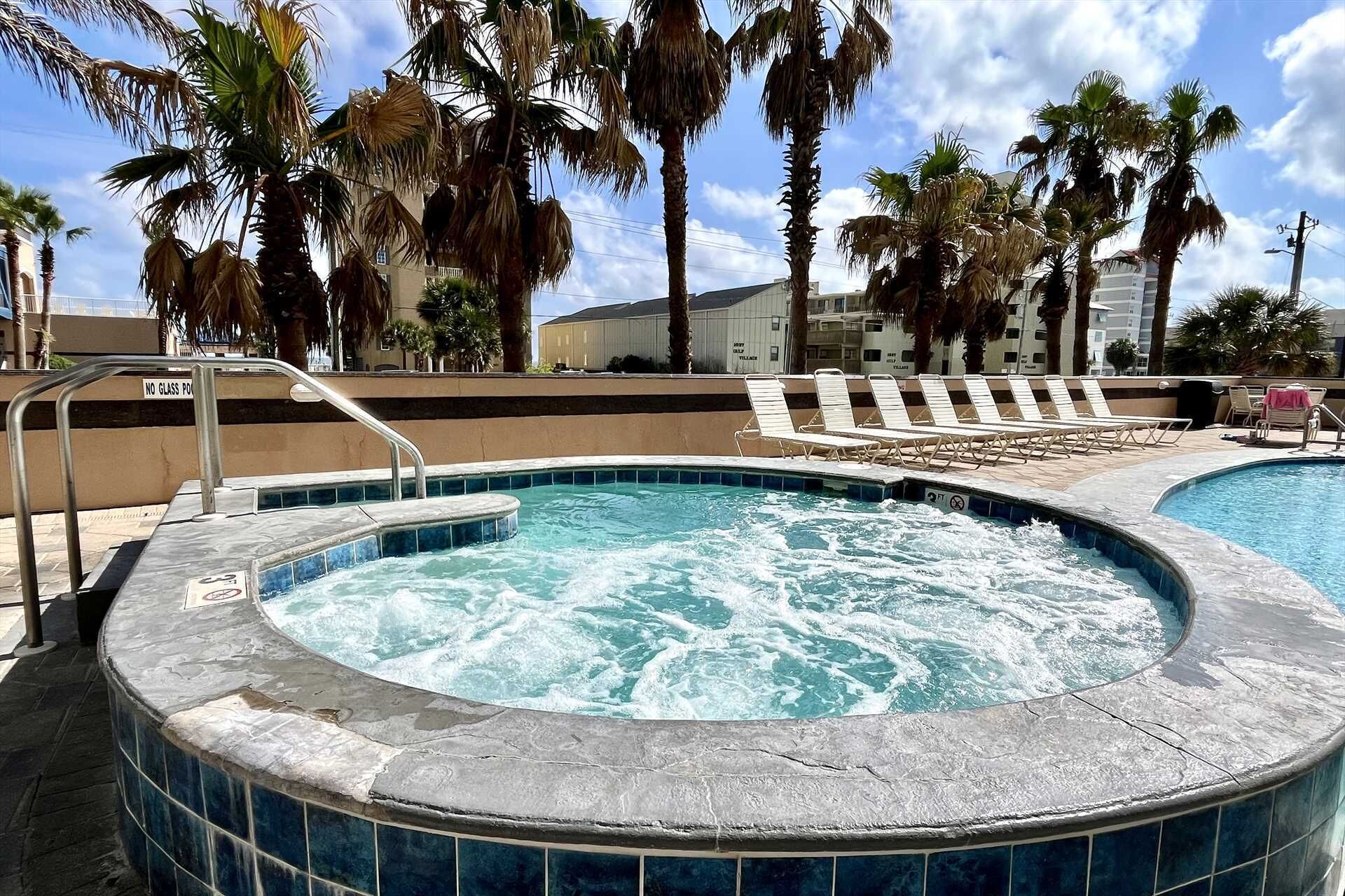 A hot tub surrounded by lounge chairs, palm trees, and a pool.