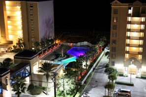 A hotel with a swimming pool surrounded by palm trees and a parking area.