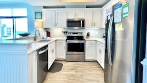 Una cocina moderna con armarios blancos, electrodomésticos de acero inoxidable y vistas de la ciudad a través de amplias ventanas.