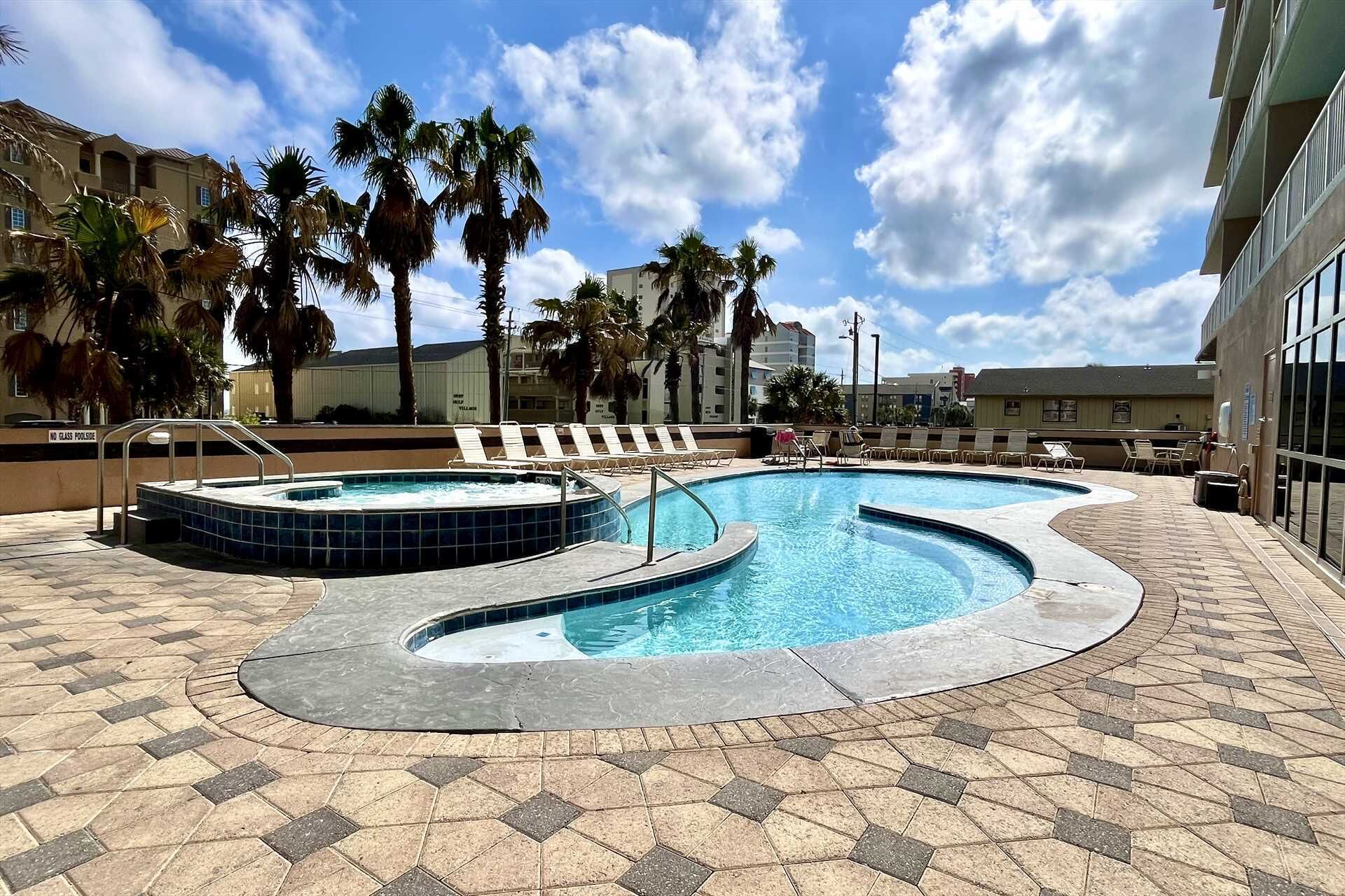 A swimming pool with a hot tub, lounge chairs, and palm trees.