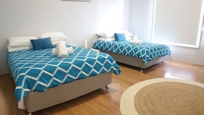 Two beds with geometric patterned bedding, a wooden floor, and a woven rug. - Vincentia Breeze by Experience Jervis Bay (Vincentia)